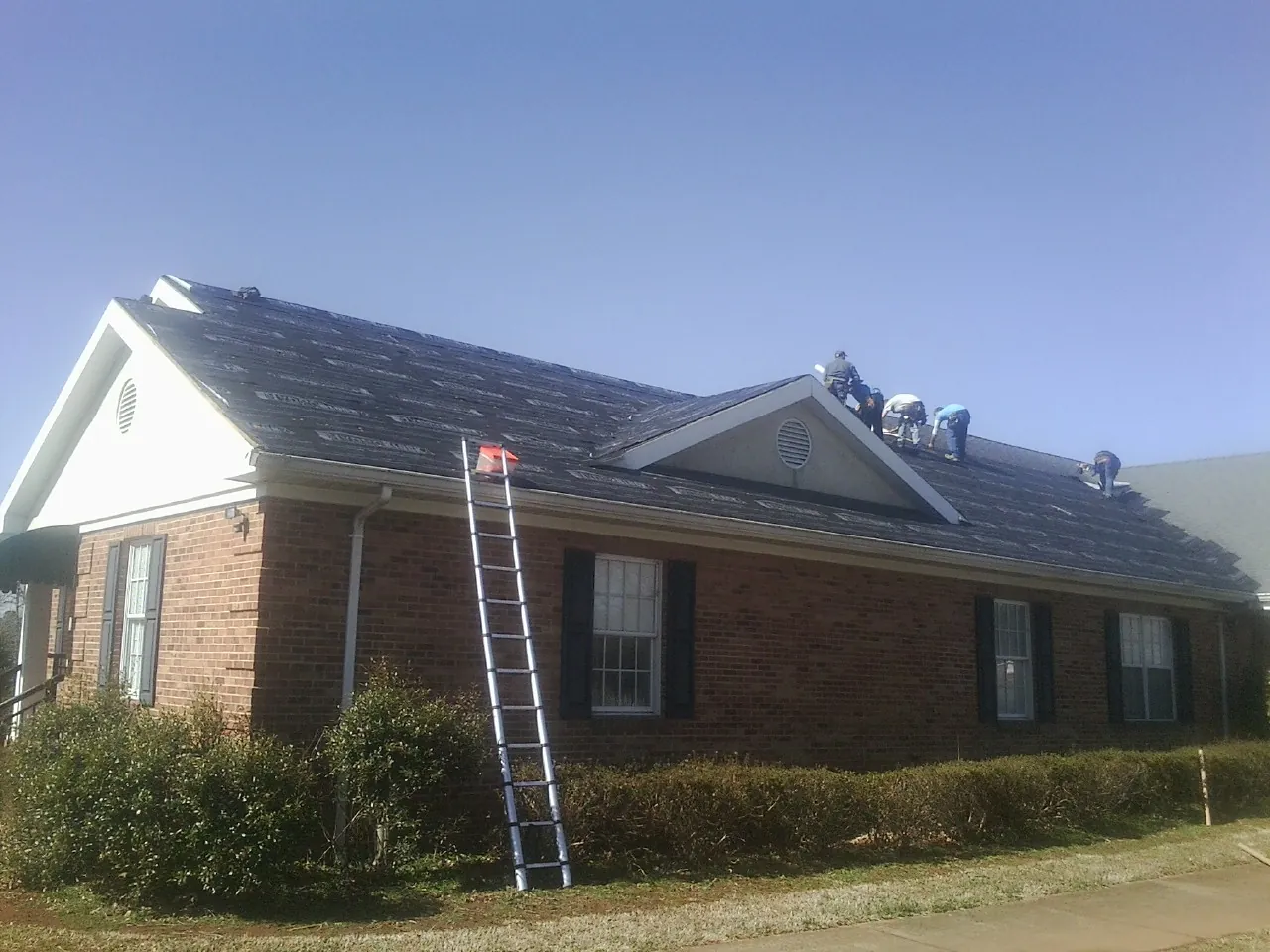Crew tearing shingles off a brick ranch roof with a ladder set — Emergency Roof Repair work by our crew in O Brien