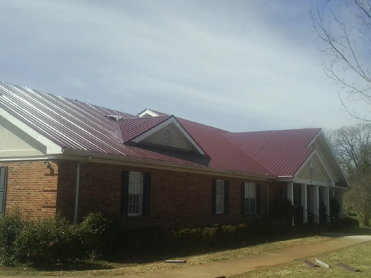 Red metal roof with gabled entries on a long brick building, from a Hail Damage Roof Repair job in O Brien