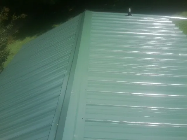 New green metal panels meeting at the ridge of a roof — Flat Roof Repair work by our crew in O Brien