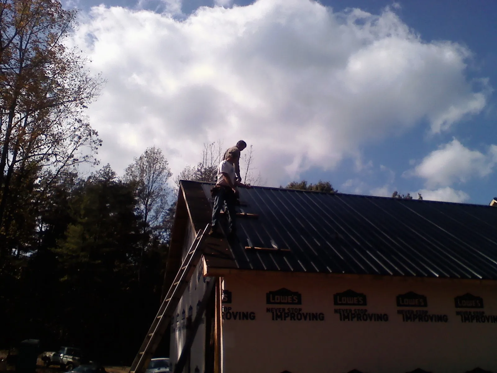 Roofer fastening dark metal panels high against a cloudy sky, from a Roof Inspection job in O Brien