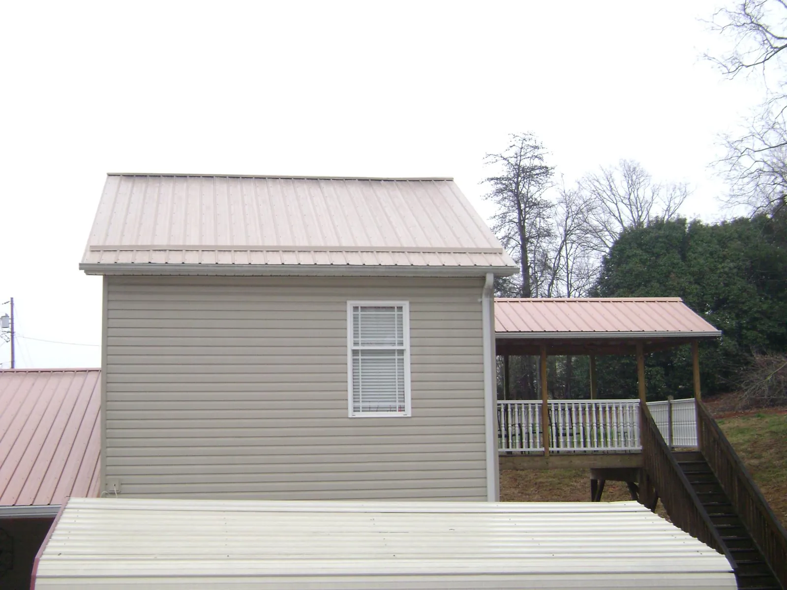 Tan metal roofs on a two story addition and attached porch, from a Roof Replacement job in O Brien